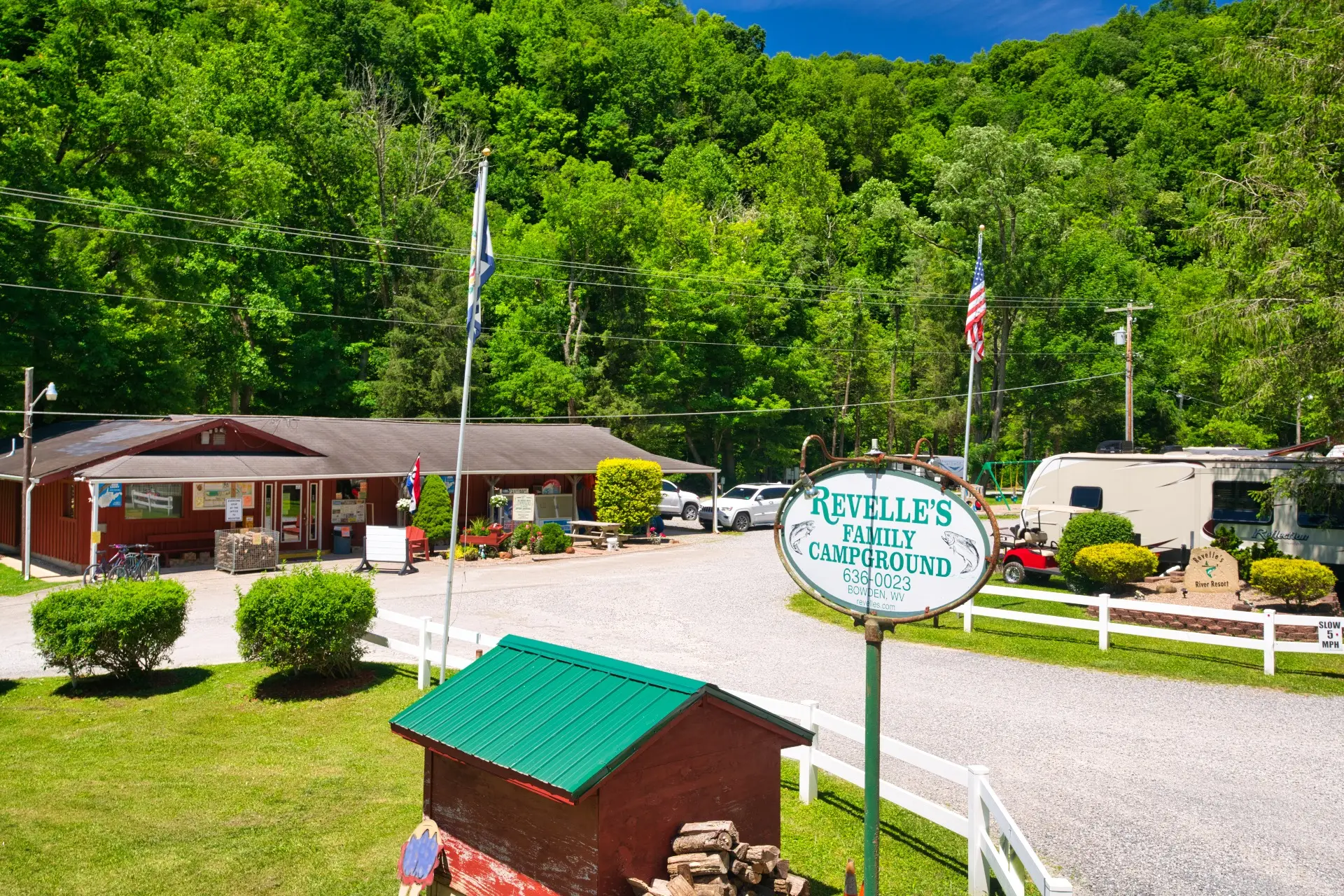 Revelle’s Family Campground entrance with sign, main office building, parked RVs, flags, and trees in the background on a sunny day.